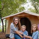 Photo of a smiling family of four (parents and two children) sitting in front of a tent at a campsite.